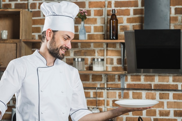 Улыбающийся шеф-повар, держащий пустую белую тарелку под рукой