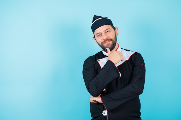 Smiling chef is looking at camera by showing perfect gesture on blue background