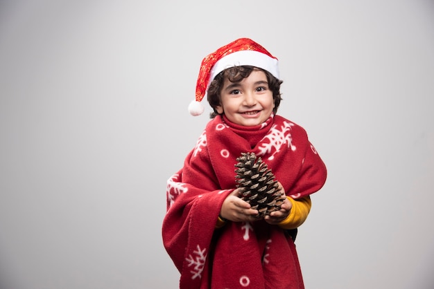Smiling child in red uniform and hat holding pinecone