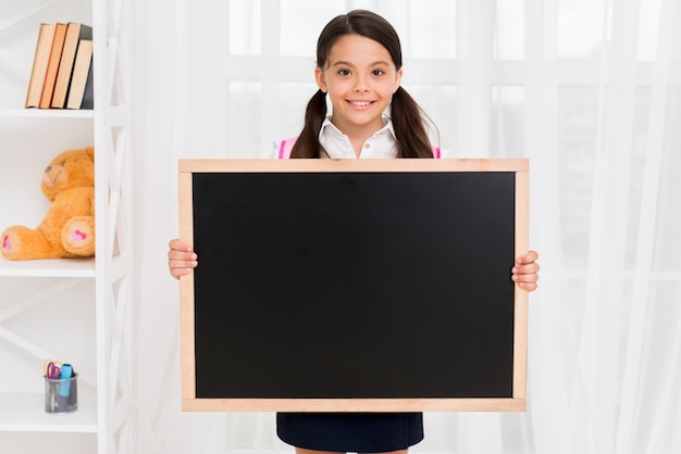 Smiling child in school uniform showing blackboard in classroom