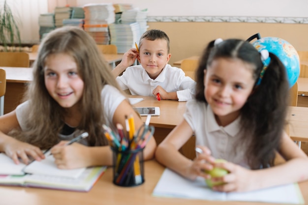 Улыбающиеся дети, сидящие в классе на столах.