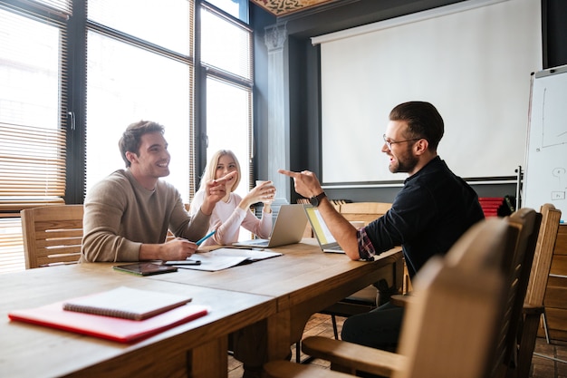 Free photo smiling colleagues sitting near coffee while work with laptops