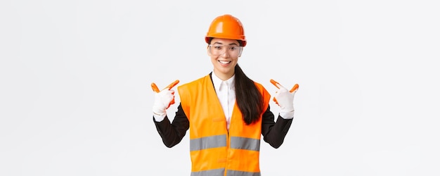 Smiling confident asian female chief construction engineer in safety helmet gloves and glasses point