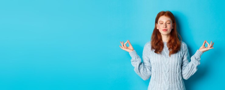 Бесплатный Фотография улыбающаяся уверенная в себе девушка с рыжими волосами остается терпеливой, держась за руки в позе дзен-медитации и старин