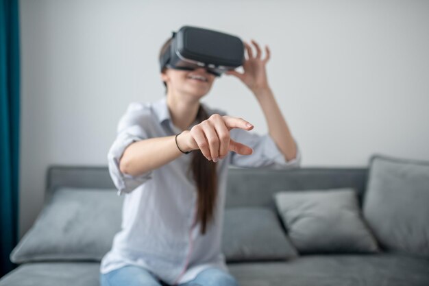 가상 현실을 탐험하는 거실에 앉아 VR 고글을 쓴 만족스러운 미소를 짓는 여성