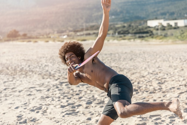 Smiling cool black guy playing beach tennis