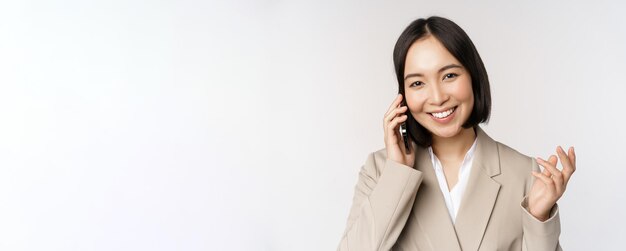 Smiling corporate woman in suit talking on mobile phone having a business call on smartphone standin