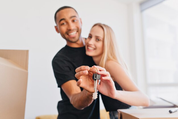 Smiling couple bought new house, holding keys for new home, moving in, packing boxes, relocating. Focus on keys.