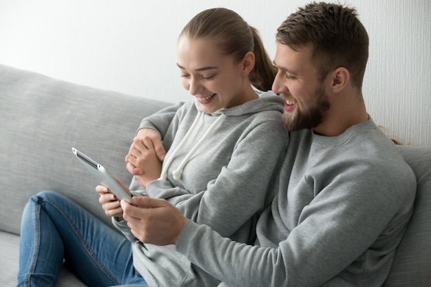 Улыбаясь пара, охватывающей с помощью планшета вместе на диване у себя дома