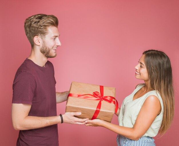 Smiling couple holding wrapped gift box against pink background