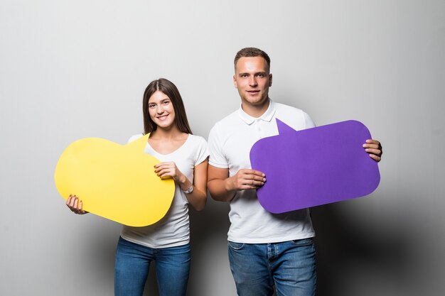 Smiling couple holding yellow and blue chat clouds in their hands isolated on white background