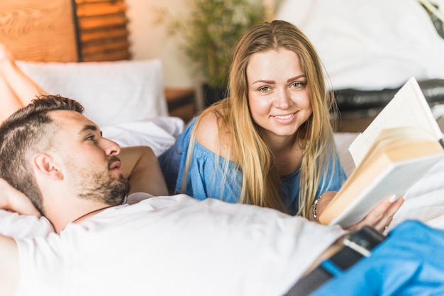 Free photo smiling couple lying on bed reading book