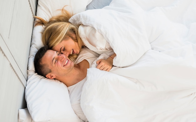 Smiling couple lying under blanket on bed