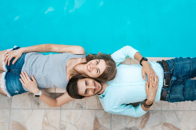 Smiling couple portrait lying dressed near the pool. They adore eachother