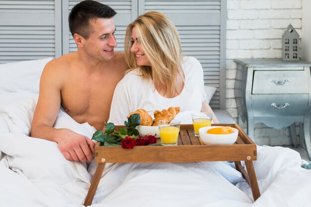 Smiling couple sitting on bed near breakfast on board