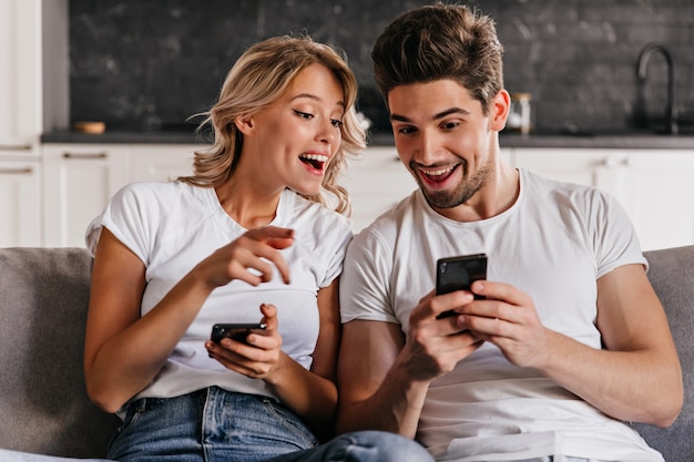 Coppia sorridente seduto sul divano con i telefoni. adorabile giovane donna che tiene smartphone.