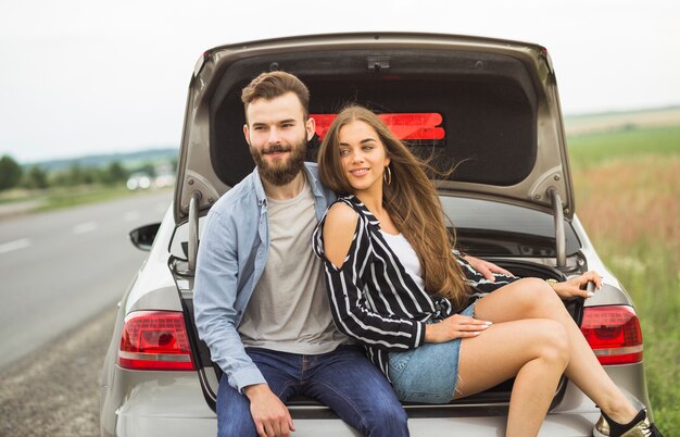 Smiling couple sitting inside the car open trunk