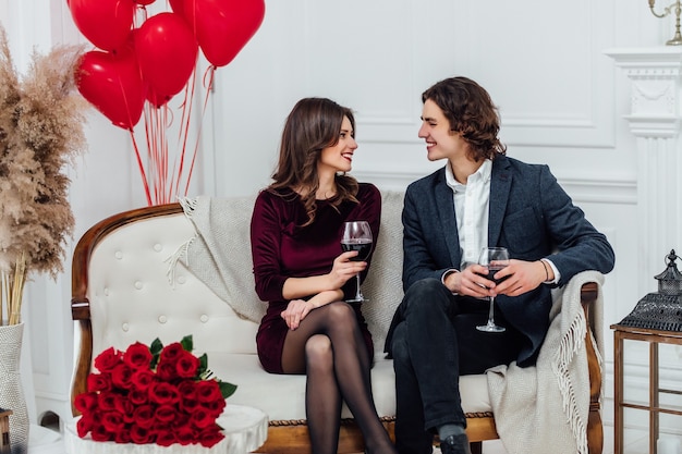 Smiling couple sitting on the sofa drinking wine and looking at each other