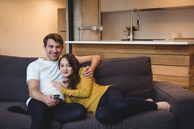 Улыбающаяся пара, сидящая на диване и смотрящая телевизор в гостиной