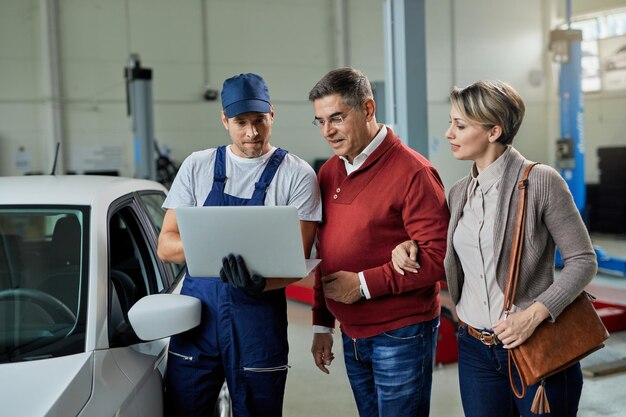 Smiling couple and their auto repairman using laptop in a workshop