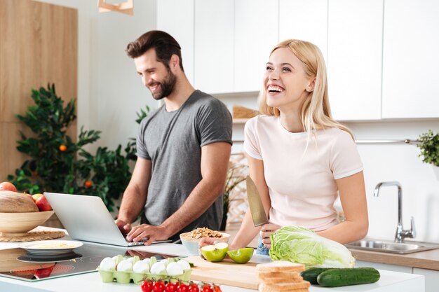 Smiling couple using notebook to cook in their kitchen