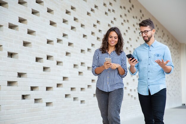 Smiling couple walking and using smartphones