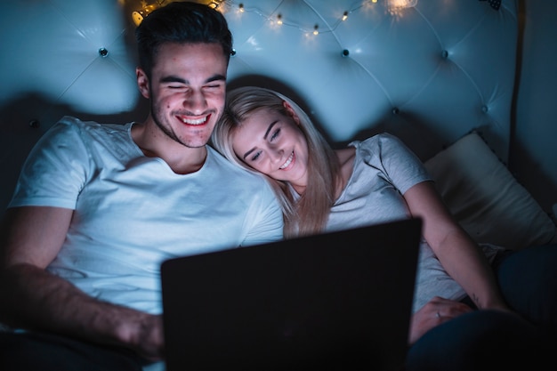 Smiling couple watching film on bed