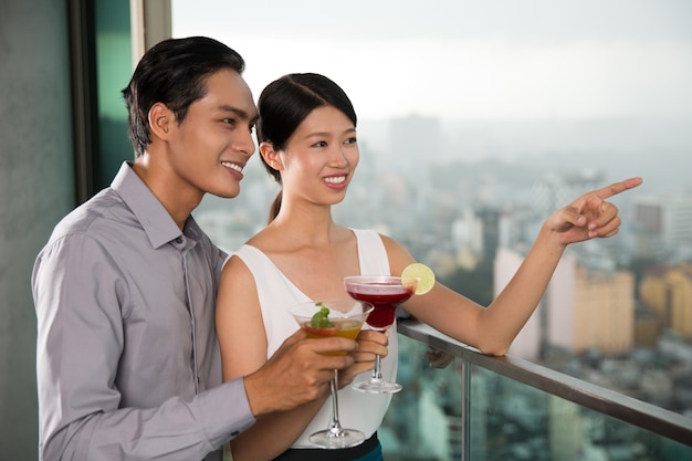 Smiling Couple with Cocktails Standing on Balcony