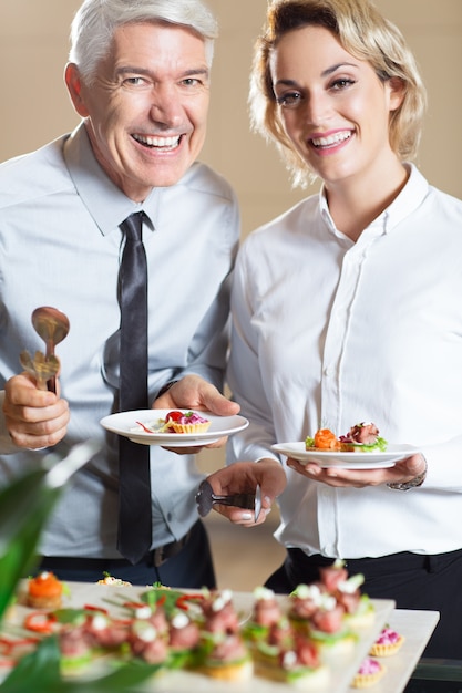 Free photo smiling couple with snacks standing in buffet