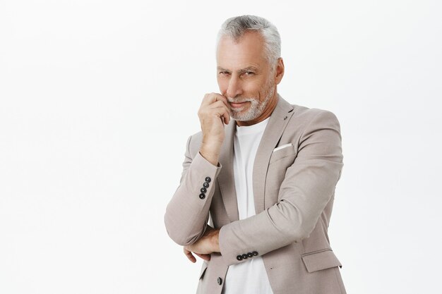 Smiling cunning senior man in suit looking intrigued and pleased over white background