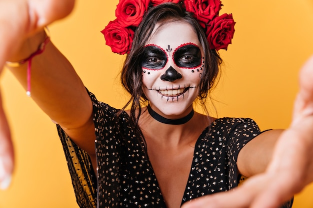 Smiling curly girl with dark hair posing. selfie model with extraordinary makeup on isolated wall