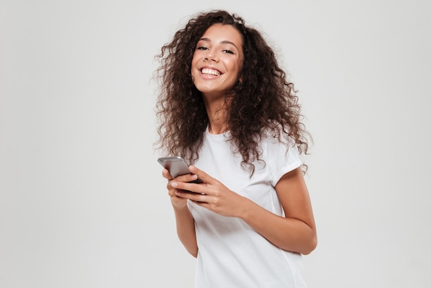 Smiling curly woman with smartphone in hands