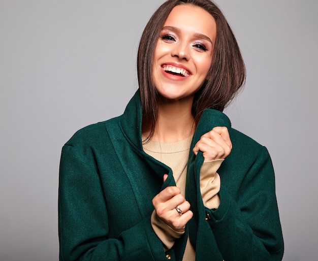 Smiling cute brunette woman in casual green jacket on gray