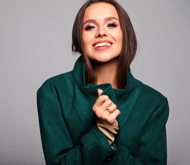 smiling cute brunette woman in casual green jacket on gray