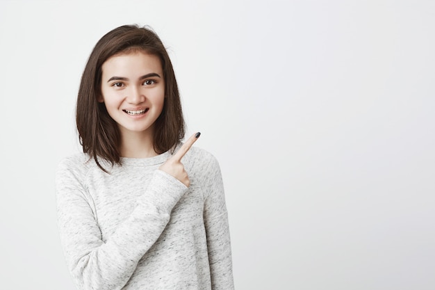 Smiling cute european woman with cheerful look, pointing at upper right corne