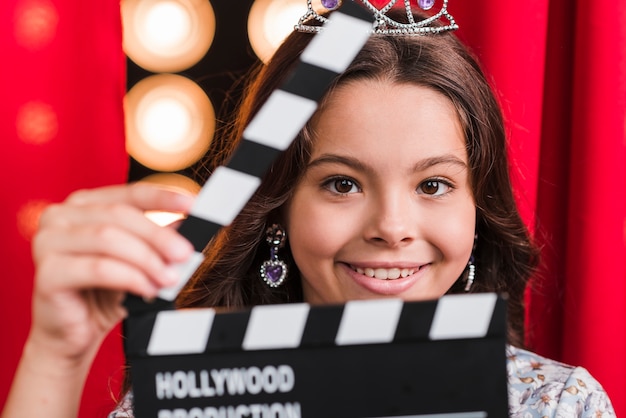 Smiling cute girl holding clapperboard