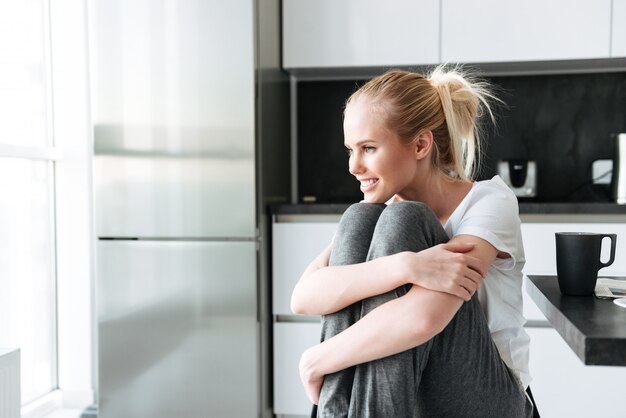 Smiling cute lady looking aside while sitting in kitchen