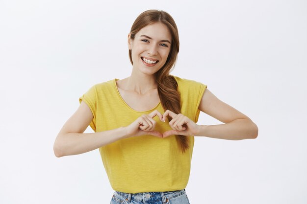 Smiling cute pretty girl showing heart gesture, express sympathy and love