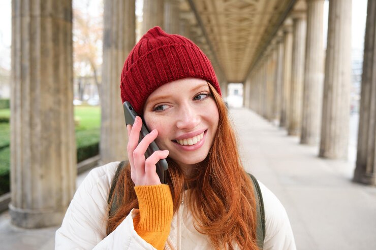 Free Photo smiling cute redhead woman makes a phone call holds telephone near year has mobile conversation usin