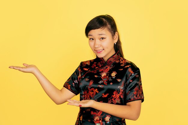 귀여운 미소, 옆에 보여주는. 행복 한 중국 새 해 2020. 노란색 배경에 아시아 젊은 여자의 초상화. 전통 옷을 입은 여성 모델이 행복해 보입니다. 축하, 인간의 감정. Copyspace.