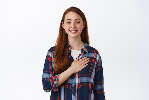 Free photo smiling cute teen girl hold hand on heart look happy feel grateful and heartfelt listen to national anthem making hontest promise white background