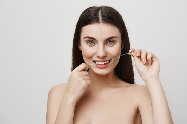 Smiling cute woman flossing teeth with dental floss