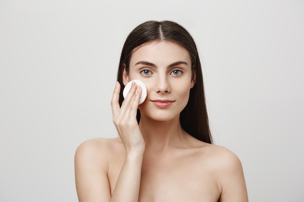 Smiling cute woman take-off makeup with cotton pad