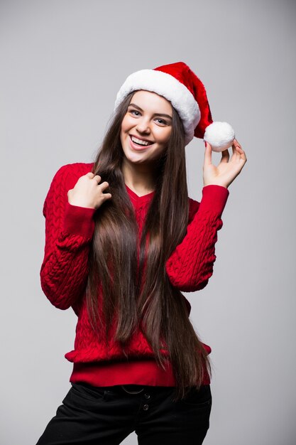 Smiling cute young woman in santa claus hat standing and looking up over gray wall