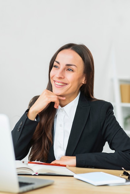 Smiling daydreaming young businesswoman sitting near the desk