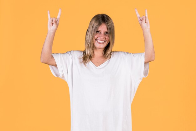 Smiling deaf woman showing rock sign in front of yellow surface