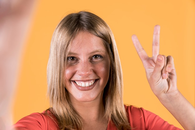 Улыбающаяся глухая женщина, показывающая знак победы над ярко-желтым фоном