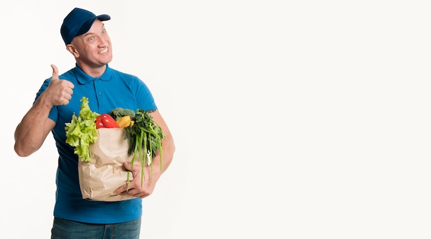 Smiling delivery man thumbs up while holding grocery bag