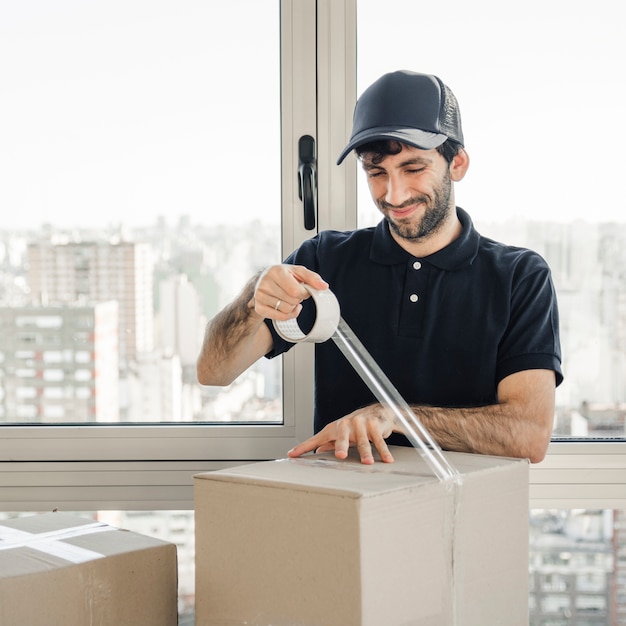 Smiling delivery man in uniform packing cardboard box