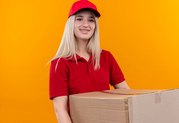 孤立したオレンジ色の背景の上の歯科ブレース保持ボックスに赤いTシャツとキャップを身に着けている笑顔